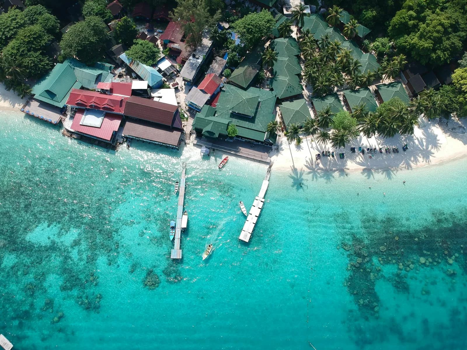 An aerial view of a Perhentian Kecil village with jetties reaching into turquoise water above coral reefs